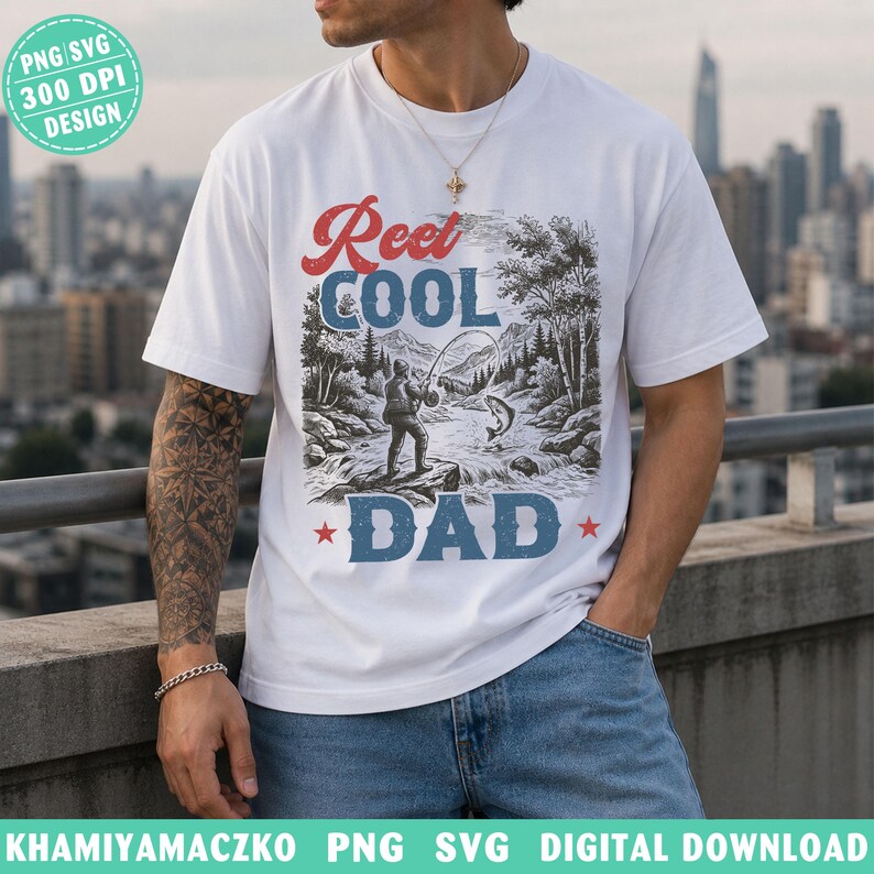 May include: White t-shirt with a graphic design featuring the text "Reel Cool Dad" in red and blue, with a fishing scene illustration. The design includes a fisherman, a fish, and a river scene.