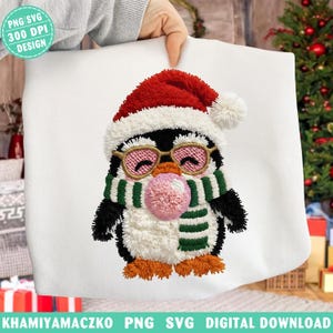 Peut inclure: Coussin blanc brodé avec un dessin de pingouin portant un bonnet de Père Noël, des lunettes et une écharpe à rayures vertes et blanches. Le pingouin a une bulle de chewing-gum rose. Le texte sur le coussin indique "PNG SVG 300 DPI DESIGN".