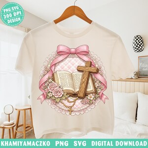 May include: A cream-colored t-shirt featuring a religious design. The design includes a pink bow, a wooden cross, an open book, roses, and a rosary. The words "PNG SVG 300 DPI DESIGN" are in the upper left corner. The words "KHAMIYAMACZKO PNG SVG DIGITAL DOWNLOAD" are at the bottom.