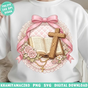 May include: White sweatshirt featuring a religious design. The design includes a wooden cross, an open book, pink roses, a rosary, and a pink bow. The design is surrounded by a pink lace-like border.