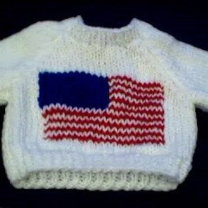 May include: White knitted baby sweater with an American flag design in red, white, and blue.