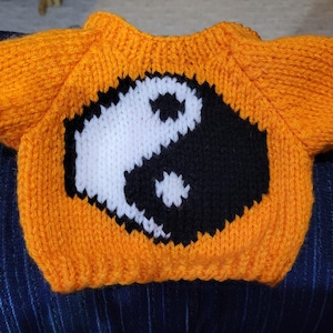 May include: Orange knitted sweater with a black and white yin yang symbol on the front.