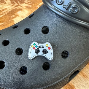 May include: A black Crocs shoe with a gray and colorful video game controller charm attached to the front.