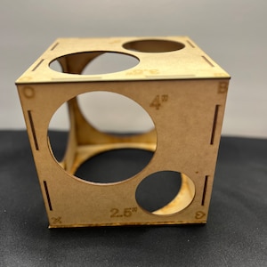 May include: Wooden box with three circular cutouts. The box is 4 inches wide and 2.5 inches tall. The box is made of light brown wood.