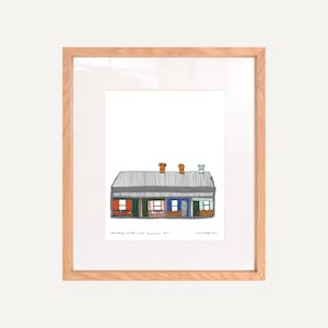 Könnte beinhalten: Eine gerahmte Illustration eines Hauses mit einem grauen Dach, orangefarbenen und braunen Schornsteinen sowie bunten Türen und Fenstern. Der Text "Queensberry Street, Melbourne 3011" und "Jane Fitzgerald" steht unter der Illustration.