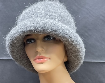 May include: A gray fuzzy cloche hat with a wide brim. The hat is made of a soft, textured material.