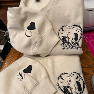 Pu&ograve; includere: Felpe girocollo beige con grafiche nere. Una felpa presenta Jack e Sally di Nightmare Before Christmas in un cuore. Le maniche hanno un cuore nero e le lettere "C" e "S".