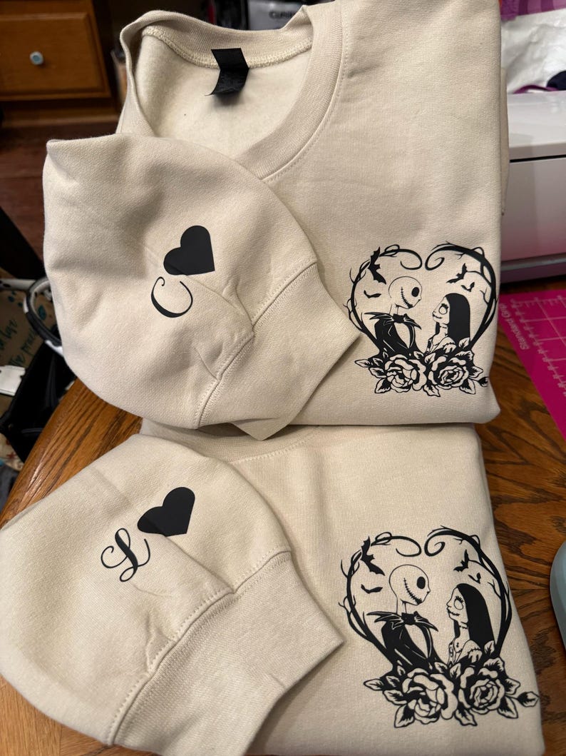 Pu&ograve; includere: Felpe girocollo beige con grafiche nere. Una felpa presenta Jack e Sally di Nightmare Before Christmas in un cuore. Le maniche hanno un cuore nero e le lettere "C" e "S".
