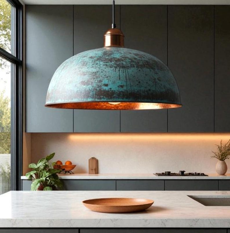 May include: A large, dome-shaped pendant light with a weathered teal finish and a copper interior hangs above a kitchen island. The light fixture is suspended from a black cord and is the focal point of the modern kitchen design.