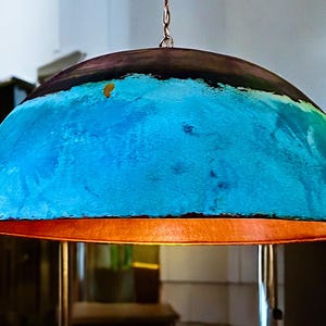 May include: A large, dome-shaped pendant light fixture with a blue and copper finish. The light is hanging from a chain and has a warm, inviting glow.