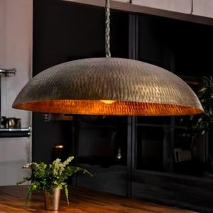 May include: A large, round, hammered metal pendant light fitting with a warm, golden glow. The light is suspended from a chain and has a textured, aged finish.