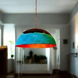 May include: A colorful, dome-shaped pendant light fixture with a blue, green, and orange paint design. The light is hanging from a chain in a room with white walls.