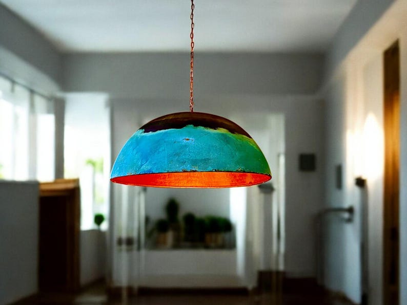 May include: A colorful, dome-shaped pendant light fixture with a blue, green, and orange paint design. The light is hanging from a chain in a room with white walls.