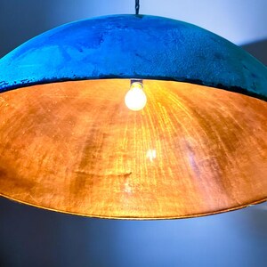 May include: A blue and copper pendant light fixture with a single light bulb. The light fixture is made of a round, dome-shaped material.