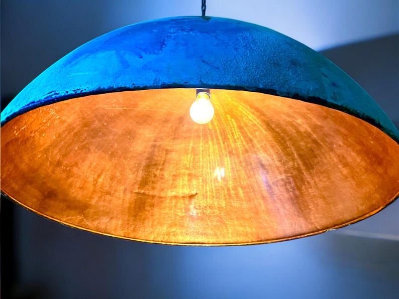 May include: A blue and copper pendant light fixture with a single light bulb. The light fixture is made of a round, dome-shaped material.