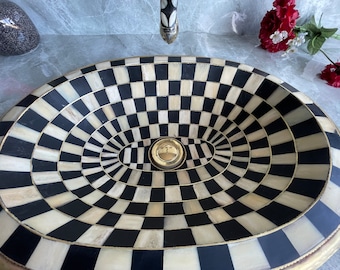 May include: An oval sink featuring a black and white chequered design. The sink has a gold-coloured drain and trim. This decorative bathroom fixture is a striking design element.
