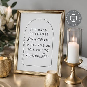 May include: A gold-framed printable sign with a black arch design and the text "It's hard to forget someone who gave us so much to remember." The sign is sitting on a table with a gold candle holder and a lit candle.