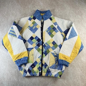 May include: A quilted jacket with a geometric pattern in white, blue, yellow, and green. The jacket has a high collar, a zip closure, and a quilted texture. The sleeves and collar feature patterned fabric.