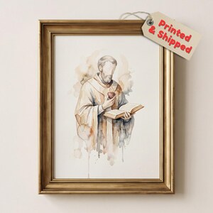 May include: A framed watercolor print featuring a bearded figure in robes holding an open book and a heart, with a tag attached to the top right corner that reads Printed & Shipped in red text. The frame is gold with a classic, ornate profile.
