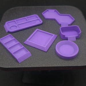 May include: A collection of purple 3D-printed trays and containers. The set includes rectangular, square, and circular shapes, as well as a tray with multiple compartments. The items are arranged on a dark surface. The text "King Ant Designs" is visible.