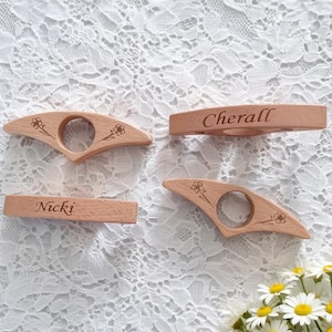 Pode incluir: Quatro anéis de guardanapo de madeira clara com acabamentos lisos. Dois anéis apresentam desenhos florais gravados, enquanto os outros dois estão gravados com os nomes Cherall e Nicki em letra cursiva. A madeira tem uma textura natural.