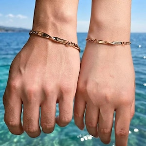 Peut inclure: Deux bracelets à chaîne de couleur or rose dotés d'une barre plate centrale. Le bracelet de gauche porte l'inscription Kim et celui de droite l'inscription Missy. Les deux bracelets présentent un design délicat à maillons métalliques torsadés.