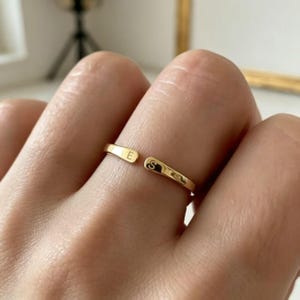 May include: A gold-toned open ring featuring two flat, rounded ends. Each end is engraved with a single uppercase letter, specifically the letter E on one side and the letter S on the other, creating a personalised and adjustable band design.