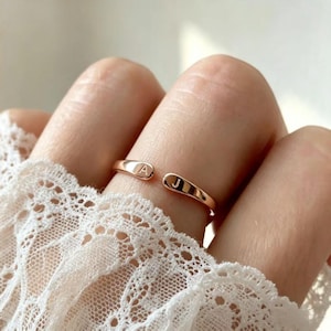 Peut inclure: Une bague ouverte en or rose avec deux extrémités arrondies, chacune gravée d'une lettre majuscule. Une extrémité porte la lettre A et l'autre extrémité porte la lettre J. L'anneau présente une finition lisse et polie au design simple.