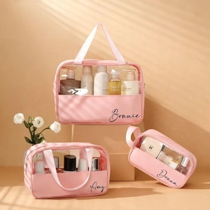 May include: Three pink cosmetic bags with clear, see-through compartments. The bags have white handles and are filled with various beauty products. The names "Bonnie", "Amy", and "Donna" are written on the bags in a cursive font.