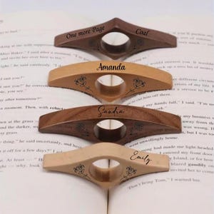 Può includere: Quattro fermapagina in legno con nomi e disegni floreali sono esposti su un libro aperto. I supporti sono in tonalità marrone e beige. I nomi "Coal", "Amanda", "Sandra" ed "Emily" sono visibili.