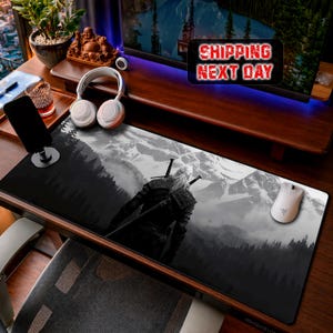 May include: Black and white gaming mouse pad featuring a mountain landscape and a figure with white hair and swords. The pad is rectangular and designed for computer use. A white computer mouse is visible on the right side.