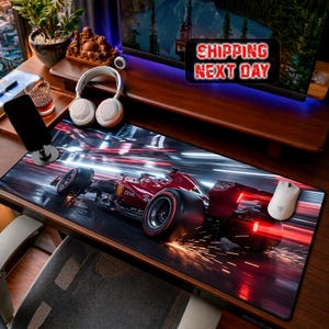 May include: A desk mat with a Formula 1 race car design, predominantly red and black, with motion blur effects. The mat also features a white computer mouse and headphones. The image includes the text "SHIPPING NEXT DAY".