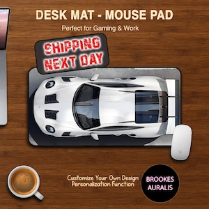 May include: A white sports car design desk mat with a matching white mouse. The mat has the text "DESK MAT - MOUSE PAD" and "SHIPPING NEXT DAY". A cup of coffee sits to the left. The mat is designed for gaming and work.