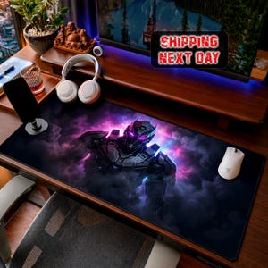 Può includere: Un ampio tappetino per mouse da gioco nero con un design robotico futuristico con accenti viola e rosa su uno sfondo fumoso. Un mouse e delle cuffie bianche sono visibili sulla scrivania di legno.
