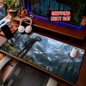 May include: A large rectangular gaming mouse mat featuring a detailed landscape with a figure holding swords. The mat has a mountain and waterfall scene with a forest. A white wireless mouse is on the right side.