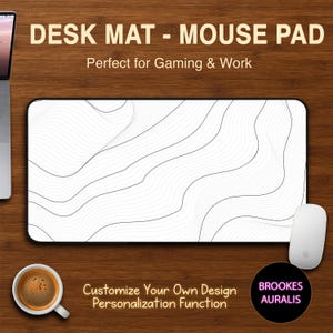 Puede incluir: Alfombrilla de escritorio rectangular con borde negro y diseño de líneas onduladas blancas y grises. El texto "DESK MAT - MOUSE PAD" está en la parte superior. También se ven un ratón blanco y una taza de café. La alfombrilla está diseñada para juegos y trabajo.