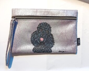 May include: A silver zippered pouch with a black poodle painted on the front. The pouch has a silver iridescent finish and the text "IPSY" is printed on the side.