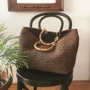 May include: A large brown woven tote bag with bamboo handles. The bag is sitting on a black wooden stool.