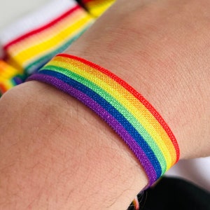 Könnte beinhalten: Ein elastisches Regenbogenarmband mit einem violetten Band. Das Armband wird am Handgelenk getragen.