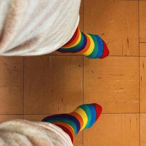 Peut inclure: Gros plan sur deux pieds portant des chaussettes rayées arc-en-ciel. Les chaussettes présentent des bandes rouges, oranges, jaunes, vertes et bleues. Les chaussettes sont associées à un pantalon clair. Un accessoire joyeux et coloré.