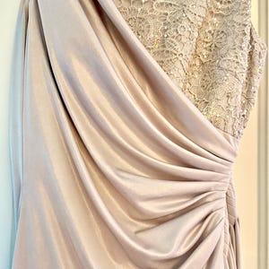 Puede incluir: Un vestido formal largo, color champ&aacute;n. El corpi&ntilde;o presenta intrincados detalles de encaje con lentejuelas, mientras que la falda drapeada est&aacute; hecha de una tela suave y fluida. El vestido tiene un dise&ntilde;o de un solo hombro y una cintura fruncida.