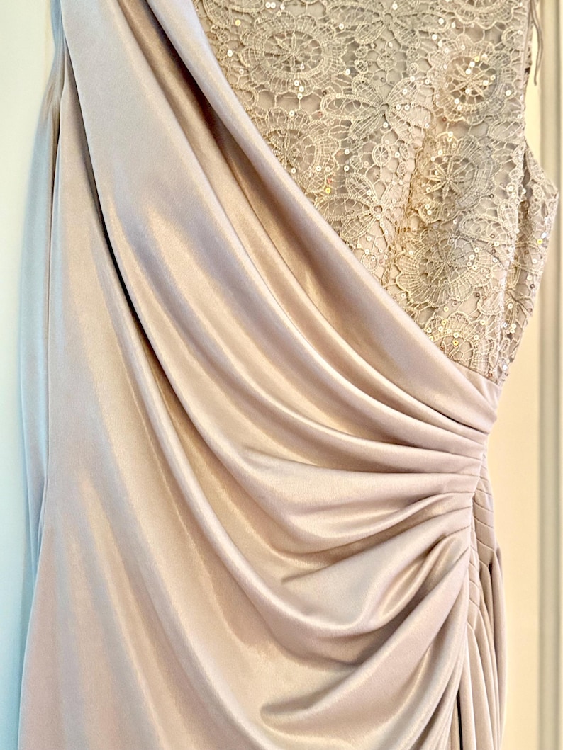 Puede incluir: Un vestido formal largo, color champ&aacute;n. El corpi&ntilde;o presenta intrincados detalles de encaje con lentejuelas, mientras que la falda drapeada est&aacute; hecha de una tela suave y fluida. El vestido tiene un dise&ntilde;o de un solo hombro y una cintura fruncida.