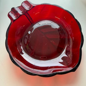 Op de afbeelding: Een levendige rode glazen kom met een gegolfde rand en een donkere rand. De kom heeft een glad, glanzend interieur en een licht getextureerde buitenkant. Het ontwerp is eenvoudig maar elegant, geschikt om te serveren of tentoon te stellen.