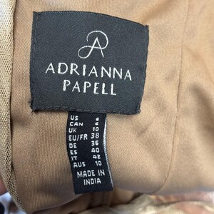 May include: A close-up of a black tag with the brand name "ADRIANNA PAPELL" in white lettering. The tag also includes size information for US, CAN, UK, EU/FR, DE, ES, IT, and AUS sizes. The tag reads "MADE IN INDIA".