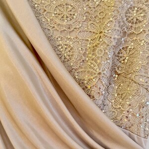 Puede incluir: Primer plano de un vestido formal con tela beige drapeada y un corpi&ntilde;o de encaje detallado. El encaje est&aacute; adornado con lentejuelas, creando un efecto brillante. El vestido tiene un dise&ntilde;o sofisticado y elegante.