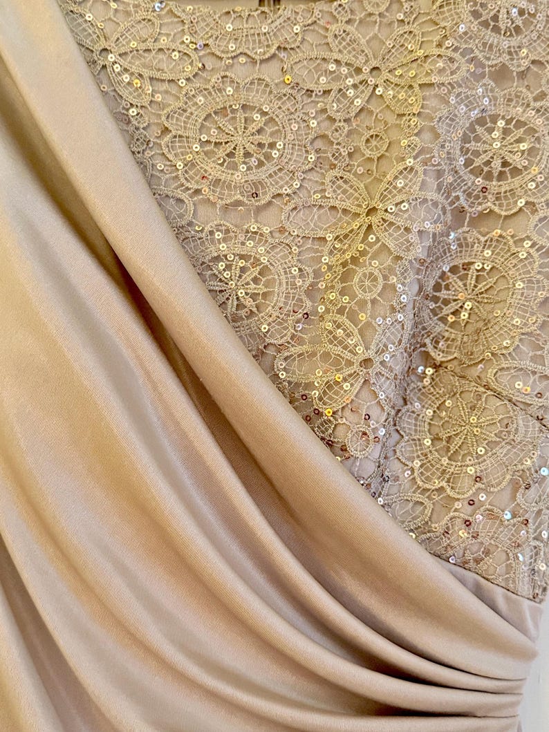 Puede incluir: Primer plano de un vestido formal con tela beige drapeada y un corpi&ntilde;o de encaje detallado. El encaje est&aacute; adornado con lentejuelas, creando un efecto brillante. El vestido tiene un dise&ntilde;o sofisticado y elegante.