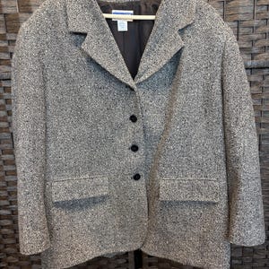 May include: A long-sleeve blazer in a speckled black and white tweed fabric. The garment features a notched lapel, three black buttons down the front, and two rectangular flap pockets at the waist. It has a dark lining and a Pendleton brand label.