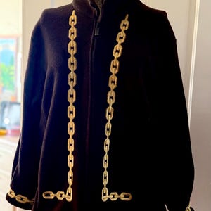 May include: Black fleece jacket with gold chain detailing. The jacket features a high collar, a full-length zipper, and gold chain accents running down the front and around the cuffs. A stylish and warm outerwear piece.