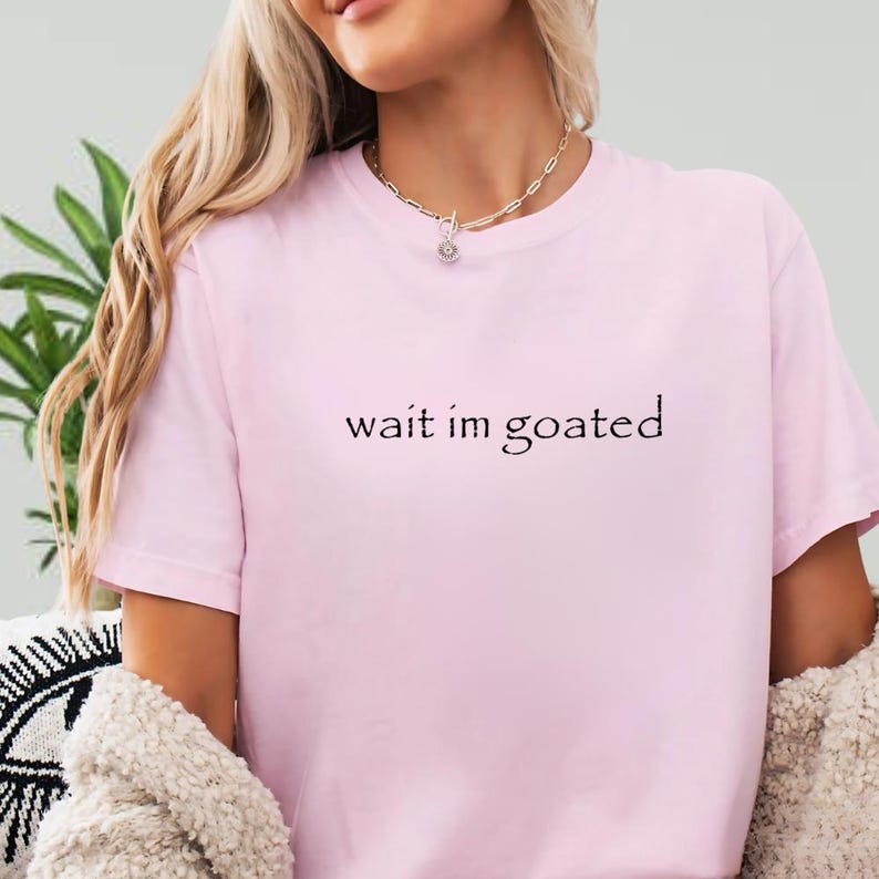 a woman wearing a pink shirt that says wait im goated