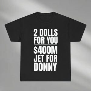 May include: Black t-shirt with white text. The text reads "2 DOLLS FOR YOU $400M JET FOR DONNY". The shirt has a crew neck and short sleeves. The text is centered on the front of the shirt.